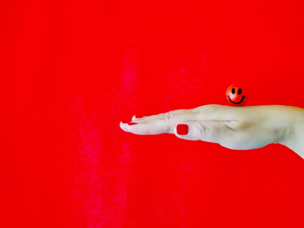 Abstract shot of woman’s hand balancing a red smiley ball against red background.